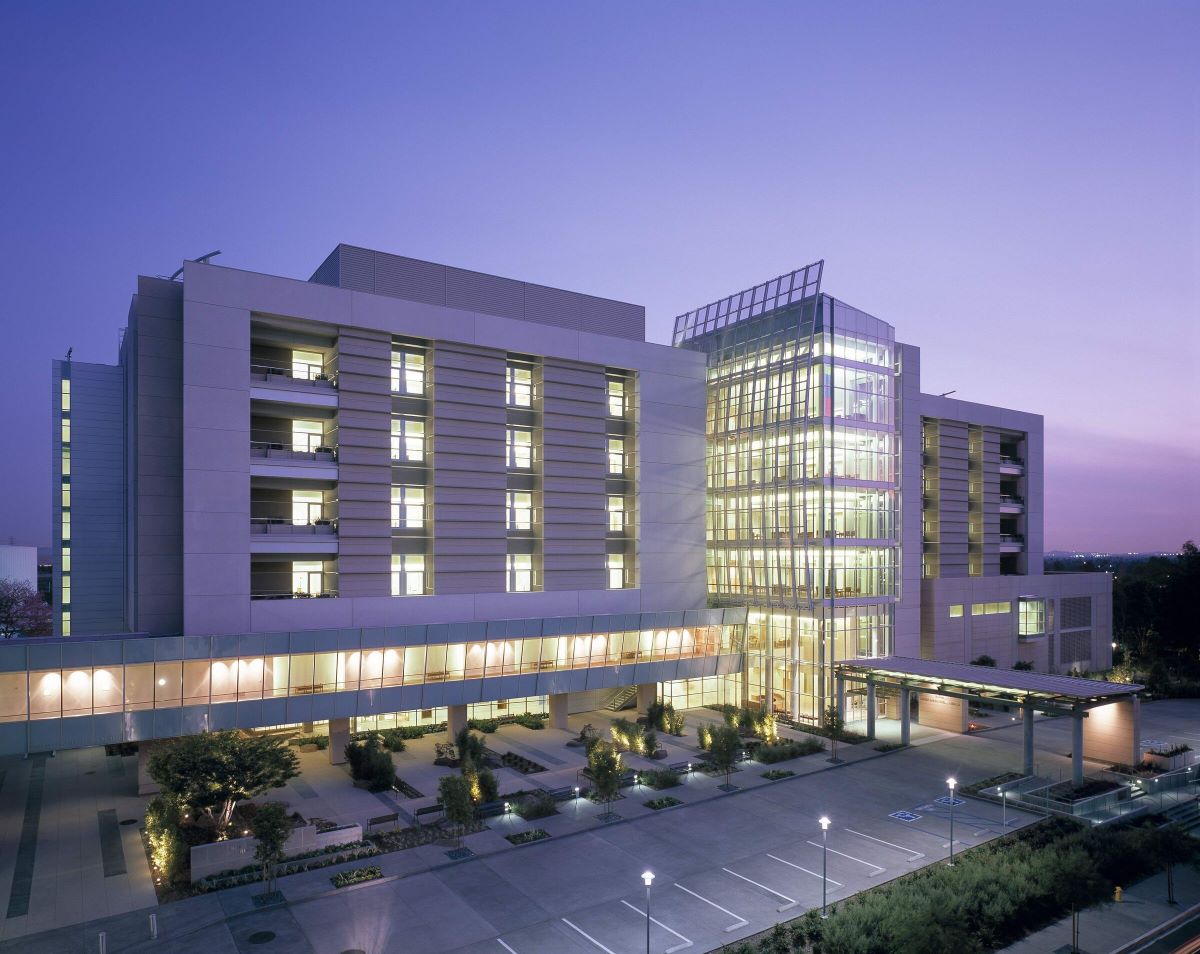 The City of Hope medical center at dusk, its glazed atrium glowing against a violet sky